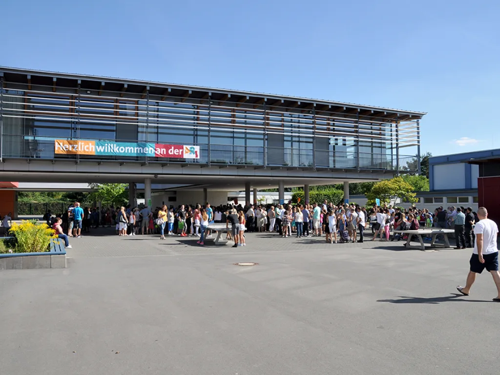 Auf dem Schulhof stehen viele Menschen unter dem Willkommensbanner.